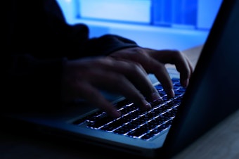 caption: A computer programmer prints a code on a laptop keyboard.