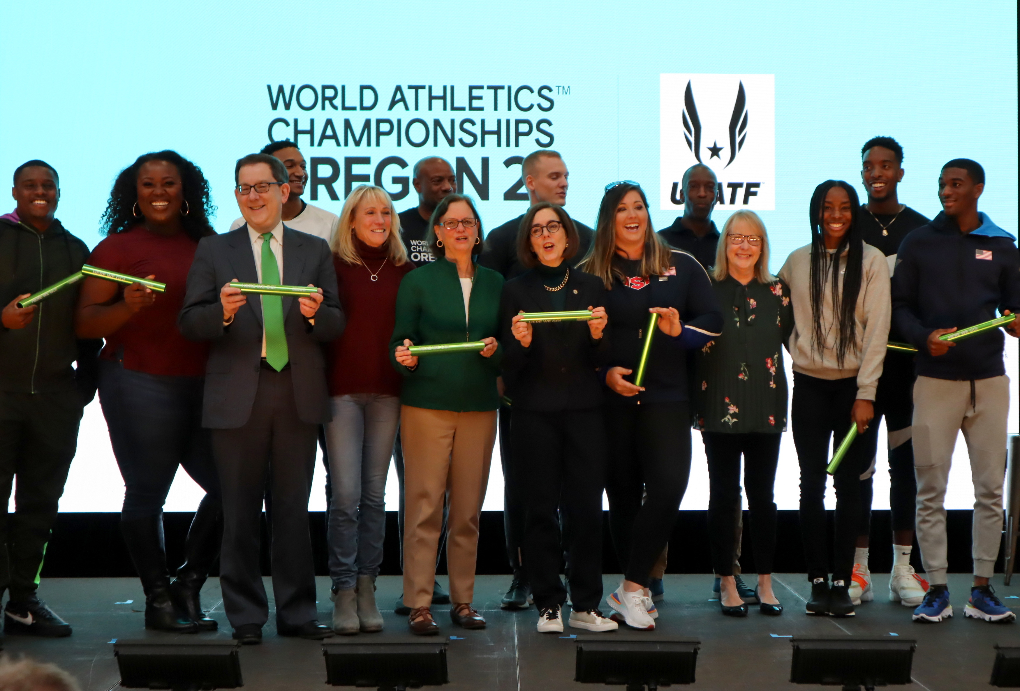 caption: Eugene Mayor Lucy Vinis, in green sweater, and Oregon Governor Kate Brown were surrounded by medal-winning Team USA athletes at an Oregon21 kickoff rally on Thursday.
