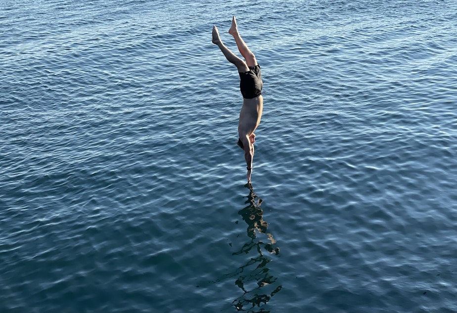 caption: A man dives into the water at Golden Gardens park in Ballard at 5:15 p.m. on Sunday, June 27, 2021, 5:15 p.m., at just about the moment when Seattle set an all-time record temperature of 104 degrees.