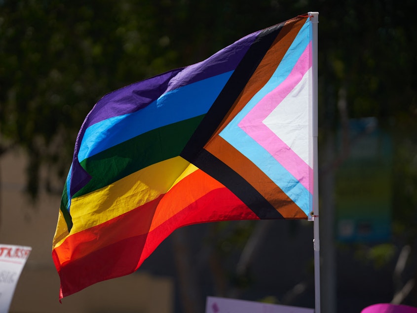 caption: A business owner was fatally shot Friday after someone allegedly took issue with a Pride flag she had displayed at her clothing store in Cedar Glen, Calif. Here, a Progress Pride Flag is held above a crowd of LGBTQ+ activists in West Hollywood, Calif., in April 2023.