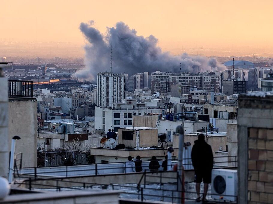 caption: A person stands on the roof of a building looking at a plume of smoke rising after a strike on Tehran, the Iranian capital, on Tuesday.