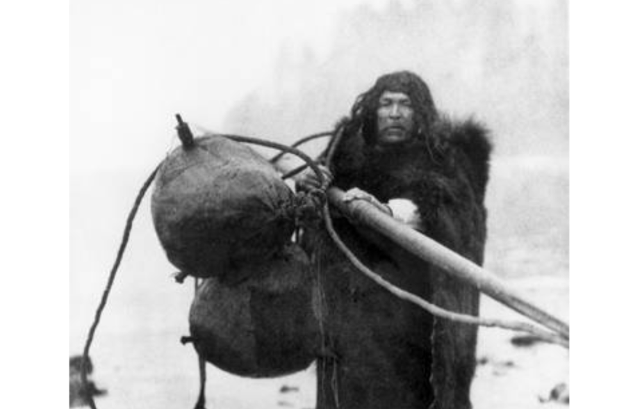 caption: A Makah whaler named Wilson Parker, 1915. Parker wears a fur coat and carries whaling floats on the beat at Neah Bay, on the northwest tip of Washington state.