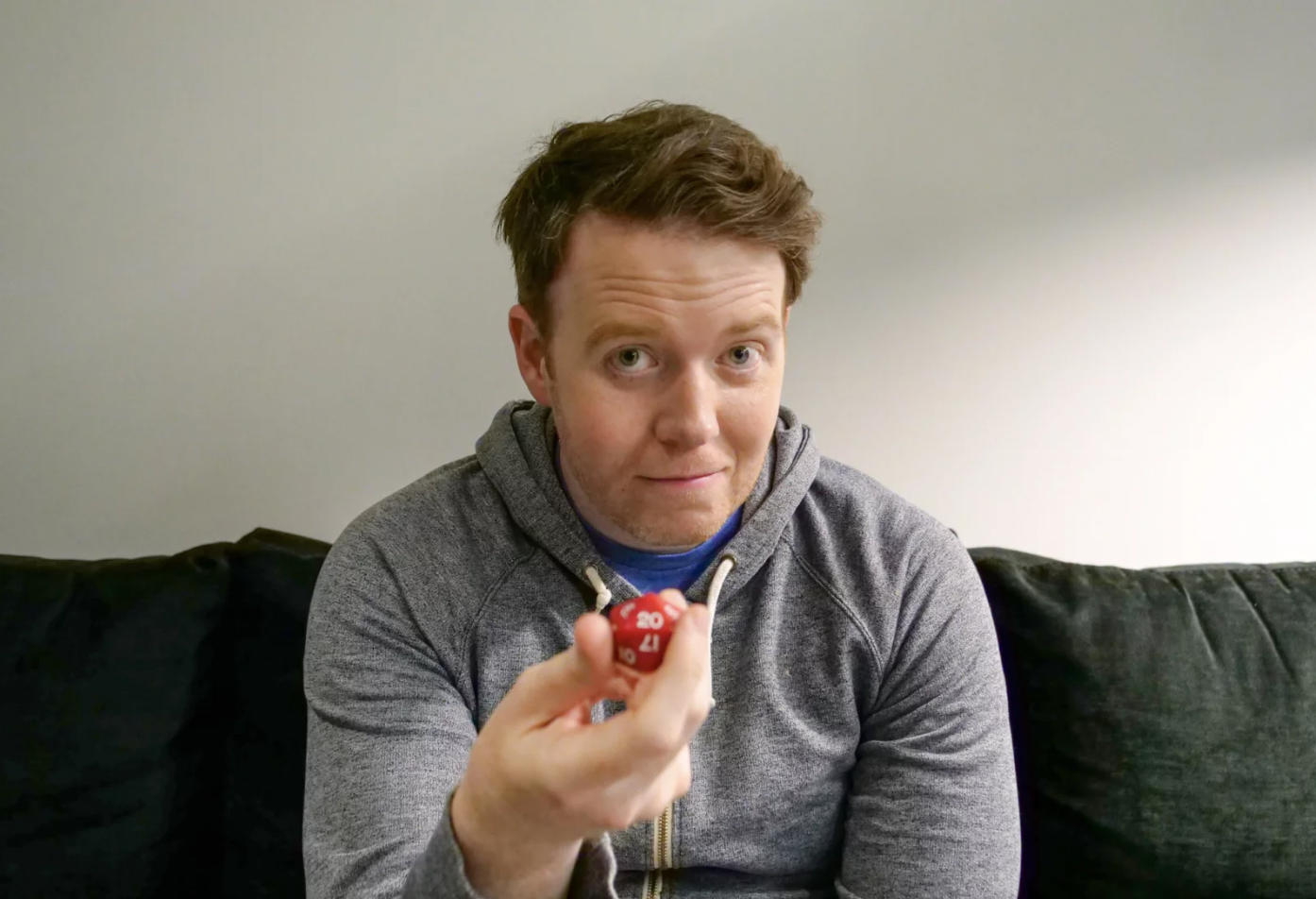 caption: Brennan Lee Mulligan holding a 20-sided die backstage at Climate Pledge Arena in Seattle after Dimension 20's performance there in July of 2025.