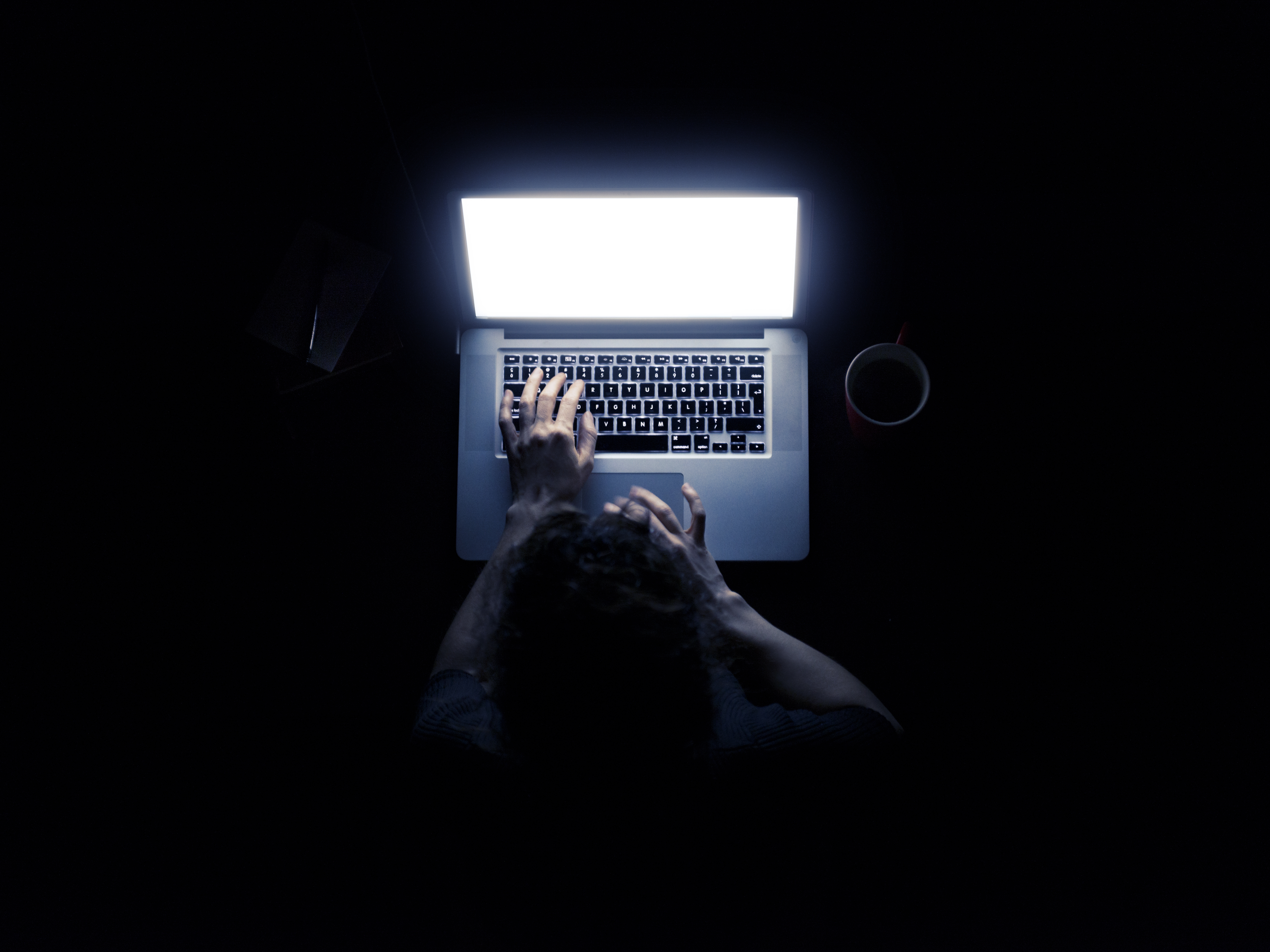 Woman using a laptop computer in darkness with her hands illuminated by the computer screen isolated on black background