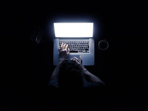 Woman using a laptop computer in darkness with her hands illuminated by the computer screen isolated on black background