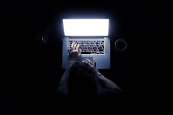 Woman using a laptop computer in darkness with her hands illuminated by the computer screen isolated on black background