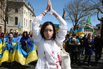 caption: A woman representing a rape victim leads protesters in Berlin demonstrating in an April 16 march against Russian military aggression in the ongoing wars in Ukraine and Syria.