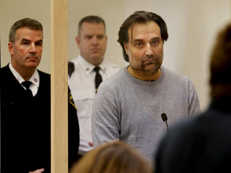 caption: Brian Walshe, center, listens during his arraignment Wednesday at Quincy District Court, in Quincy, Mass., on a charge of murdering his wife Ana Walshe.