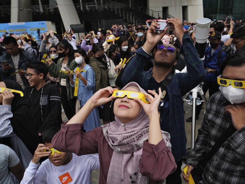 caption: People use protective glasses to watch solar eclipse in Jakarta, Indonesia, Thursday, April 20, 2023.