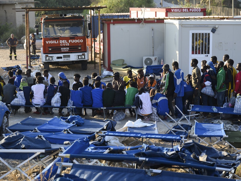 caption: Migrants are seen standing in Lampedusa's migrant reception center on Sept. 14. The reception center in Italy's southernmost island of Lampedusa has been overwhelmed in recent weeks with transferring to the mainland thousands of migrants arriving on small, flimsy boats.