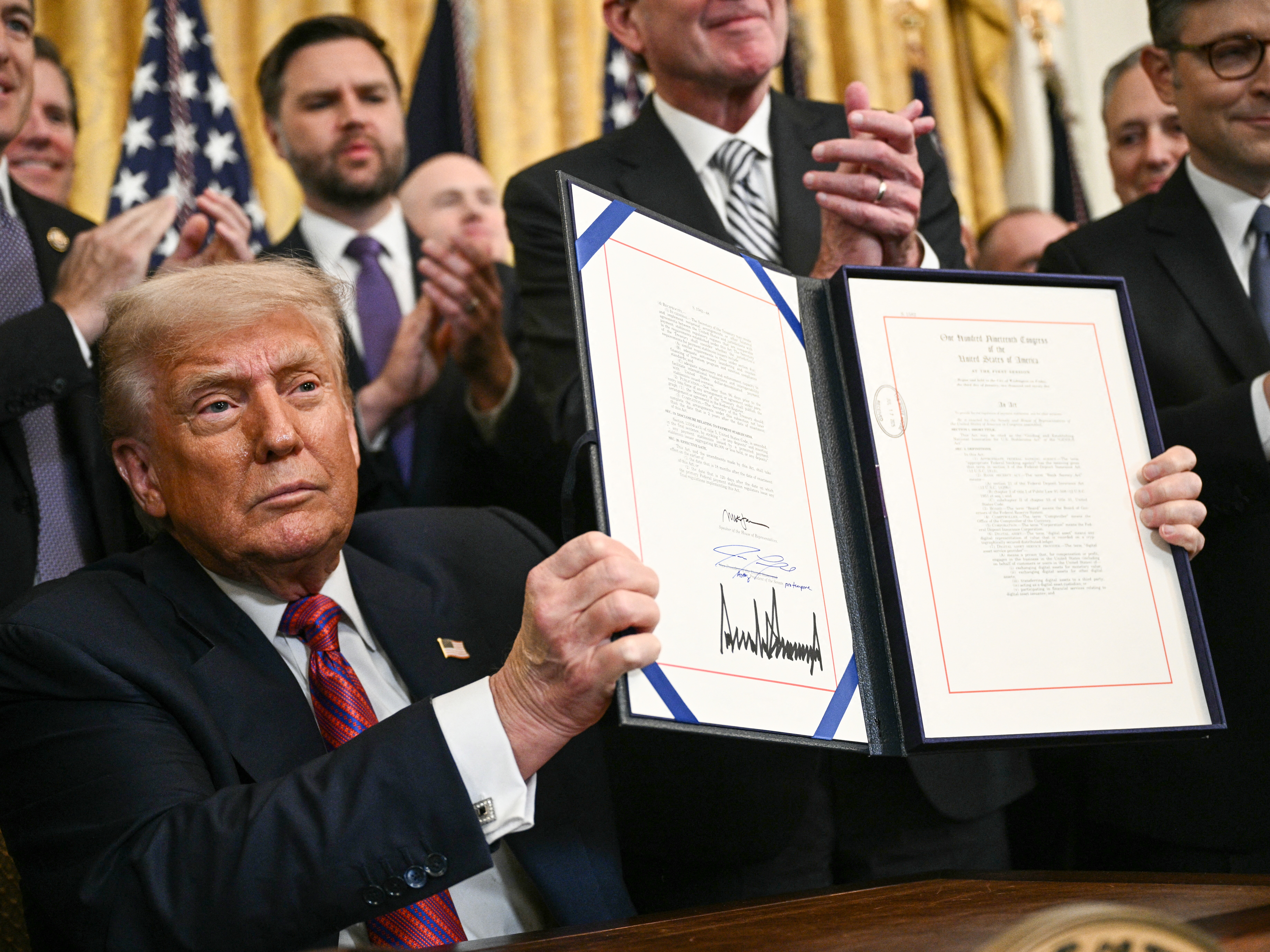 caption: President Trump displays the GENIUS Act — the first major crypto legislation passed by Congress — after signing it in the White House in Washington, D.C., on July 18, 2025.