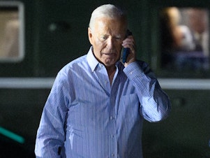 caption: President Biden speaks on the phone while walking to board Air Force One after a fundraiser in New Jersey on Saturday.