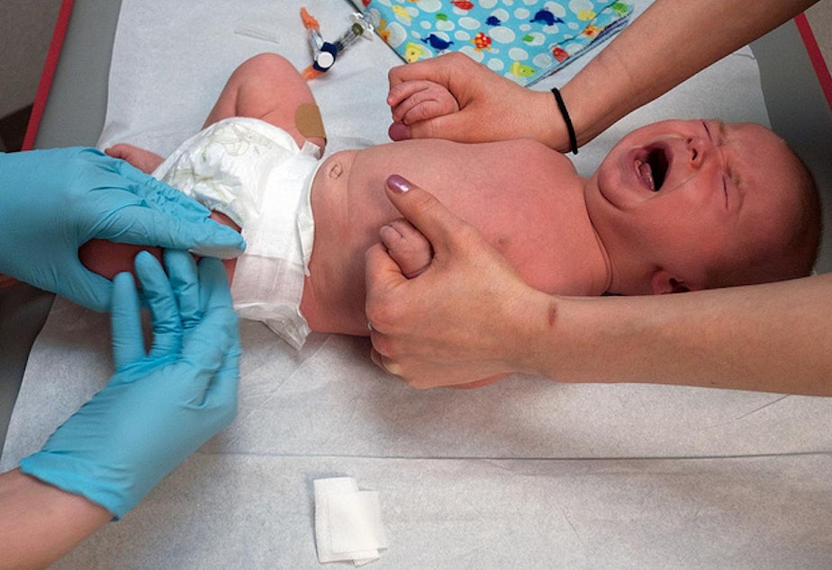 caption: Infant receives vaccination in the thigh. 