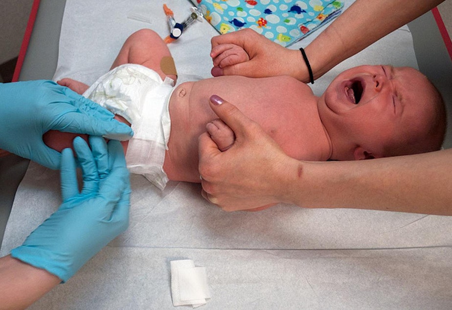 caption: Infant receives vaccination in the thigh.