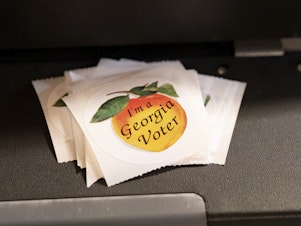 caption: A stack of stickers sits atop a ballot scanner during the midterm elections on Nov. 8, 2022, in Tucker, Georgia. In 2024, Georgia is poised to play a pivotal role in the outcome of the presidential election. 