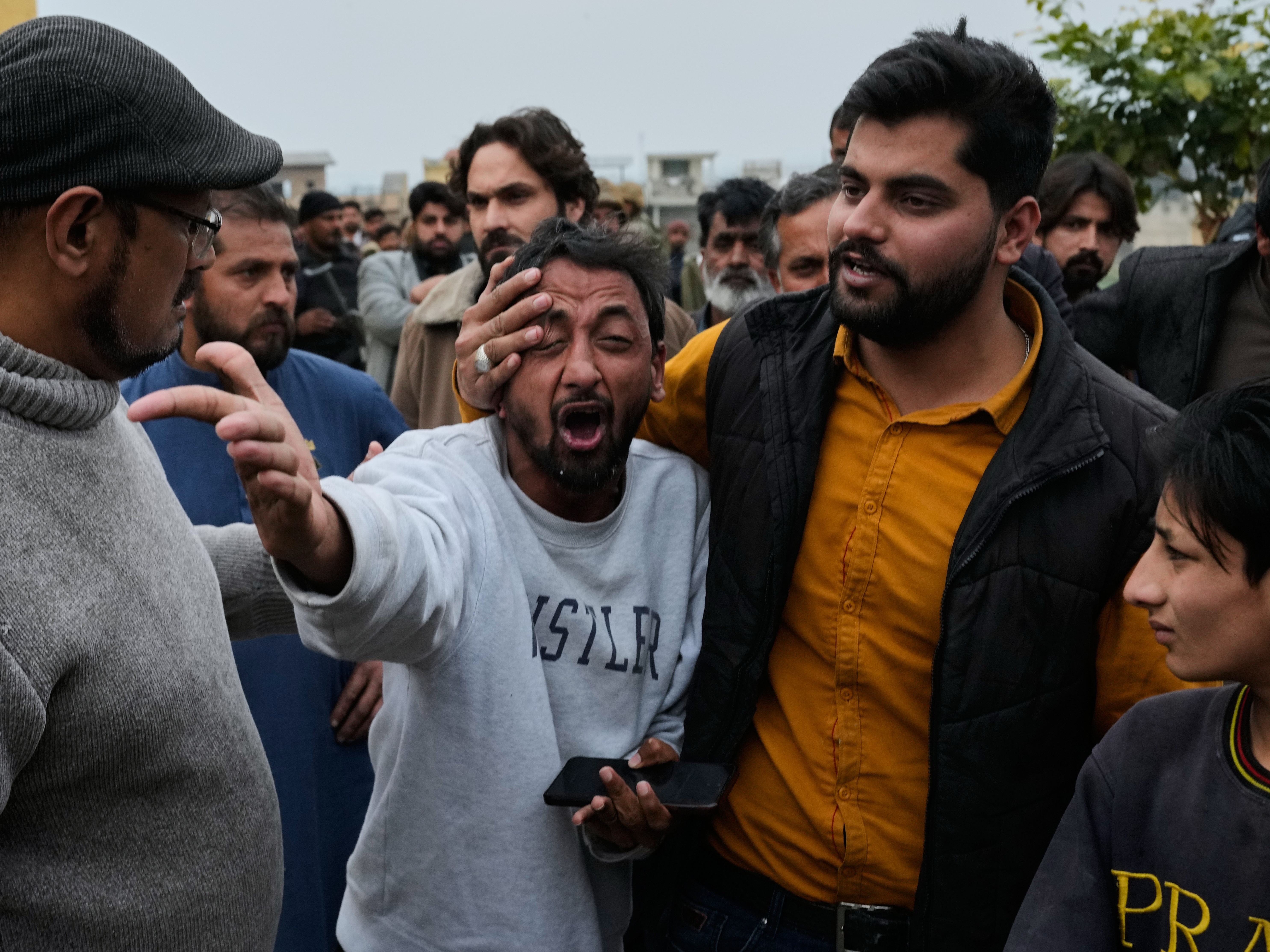 caption: People comfort a man, center, mourning over the death of his relative, close to the site of a bomb explosion at a Shiite mosque, in Islamabad, Pakistan.