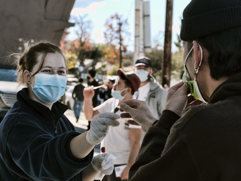 caption: A man is handed a swab for a rapid test as people line up for coronavirus testing at a gas station in the Reseda section of Los Angeles on Sunday.