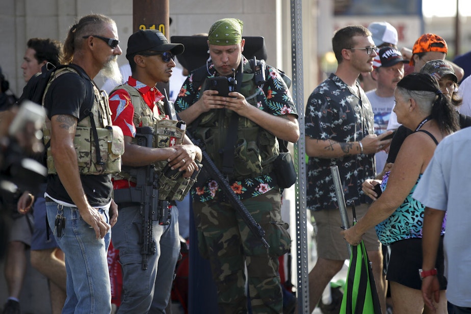 caption: Gun-carrying men wearing the Hawaiian print shirts associated with the Boogaloo movement watch a demonstration near the BOK Center where President Trump held a campaign rally in Tulsa, Okla., Saturday, June 20, 2020. 