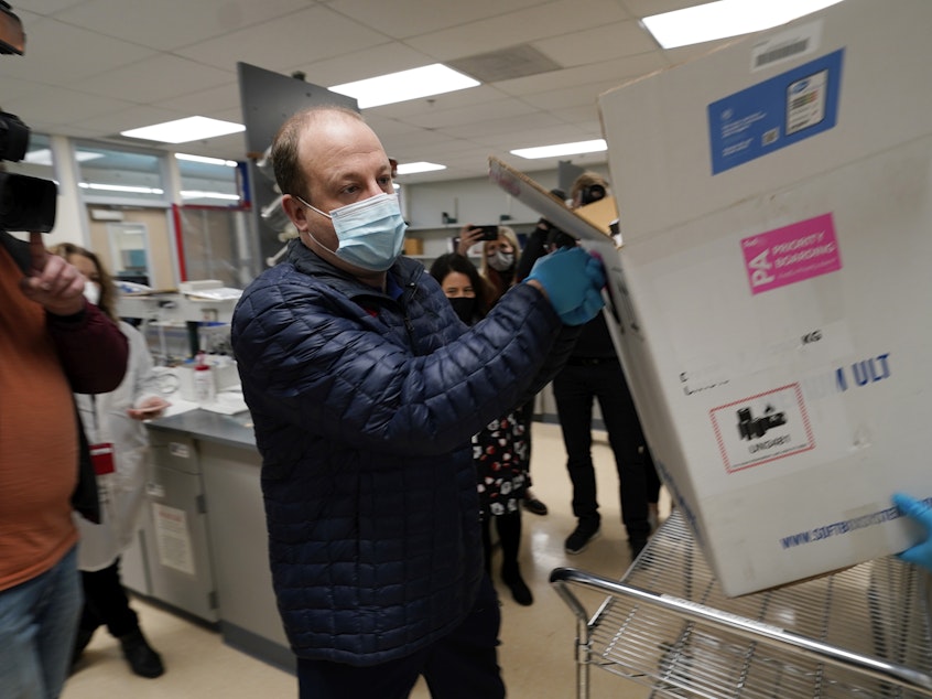 caption: Gov. Jared Polis helps put Colorado's first shipment of COVID-19 vaccine in a freezer at a state health department laboratory last week.