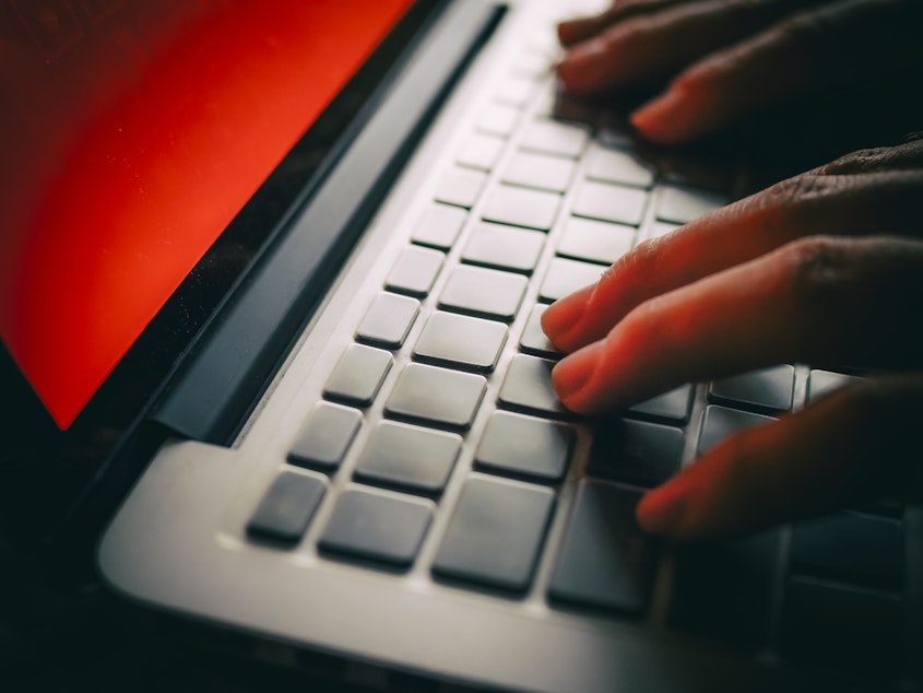 Fingers are shown typing on a laptop with a red screen