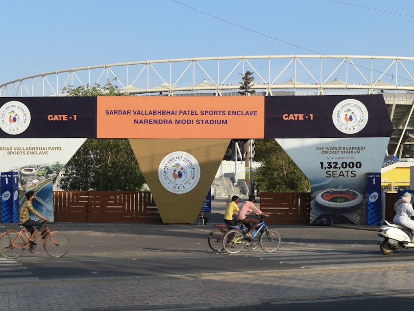 caption: Cyclists cycle past the main entrance of the Narendra Modi Stadium in Ahmedabad, India, a venue where cricket matches were taking place during the 2021 Indian Premier League — until it was suspended.