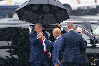 caption: Donald Trump, left, is handed an umbrella from Walt Nauta, his personal aide and co-defendant in a felony case in Florida, on Thursday, the day the former president pleaded not guilty to four felony charges in Washington, D.C.