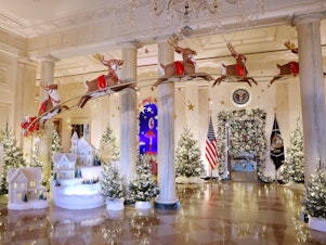 caption: Santa Claus in his sleigh and a team of reindeer fly through the columns of the Entrance Hall of the White House. The theme for this year's White House decorations is "Magic, Wonder and Joy."
