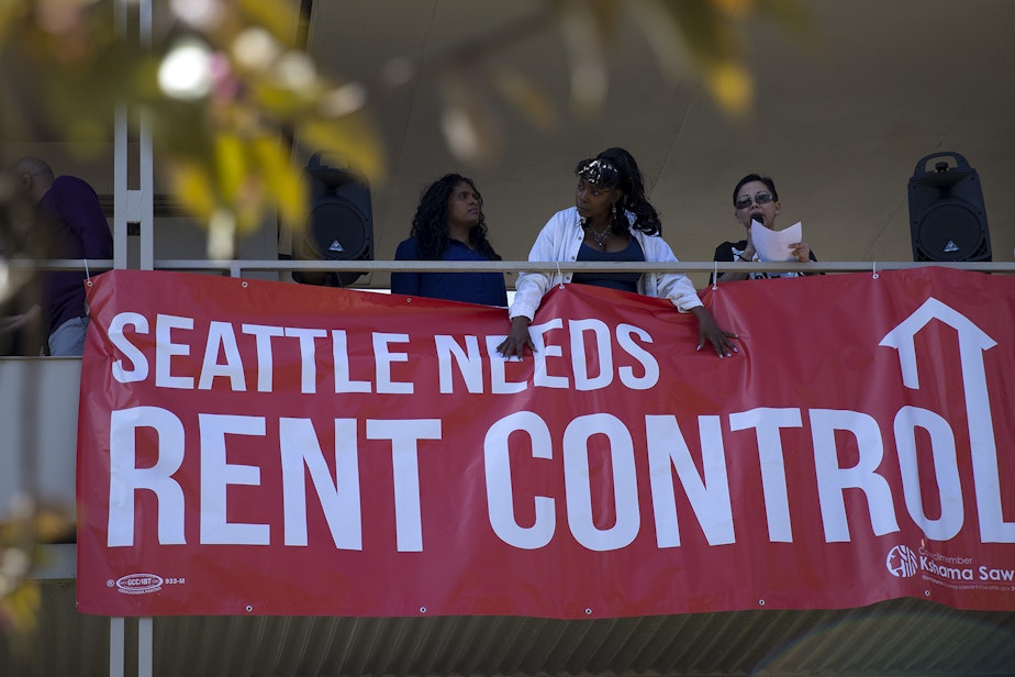 caption: Renee Gordon, center, holds down a Seattle Needs Rent Control sign at the Chateau Apartments on Wednesday, May 1, 2019, during the 20th annual May Day march near the intersection of East Fir Street and 19th Avenue in Seattle. 