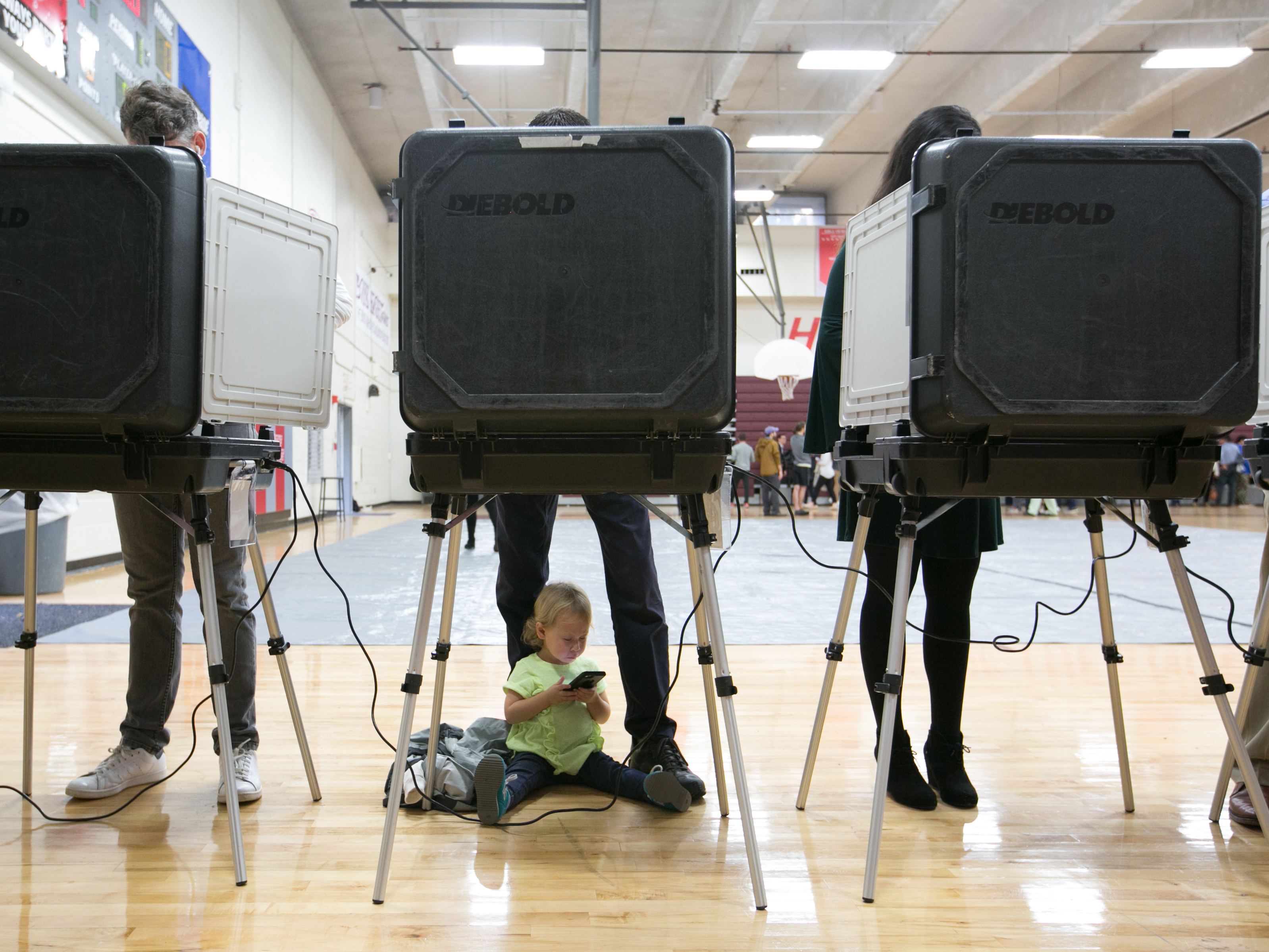 caption: A 2-year-old waits between her father's legs as he and other voters cast their ballots at a polling station set up at Grady High School in Atlanta on Election Day. The state is one of a handful that still use voting machines that don't provide a paper record.