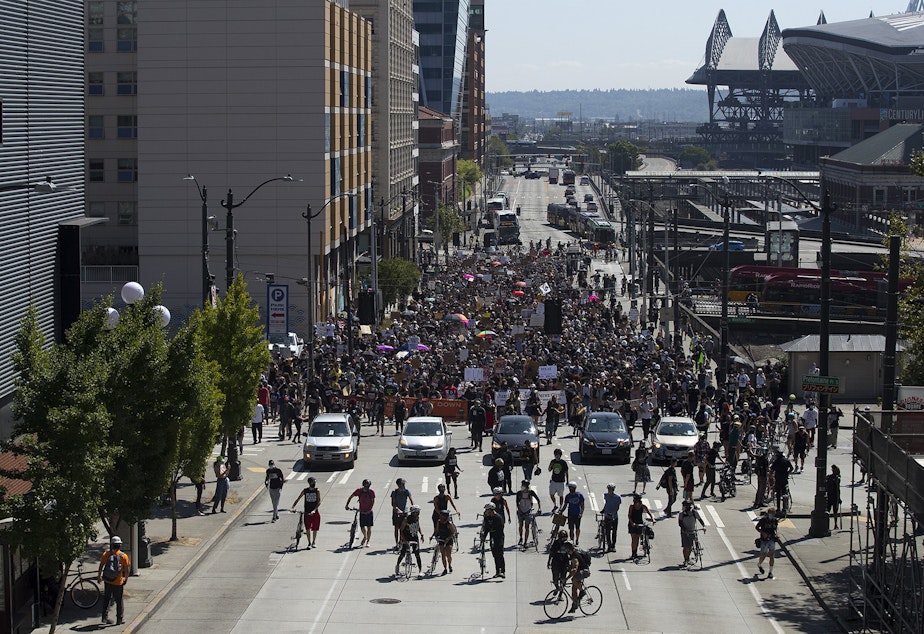 caption: A crowd of around 1,000 people march toward Seattle City Hall during a Defund The Police march from the King County Juvenile Detention Center on Wednesday August 5, 2020, in Seattle.