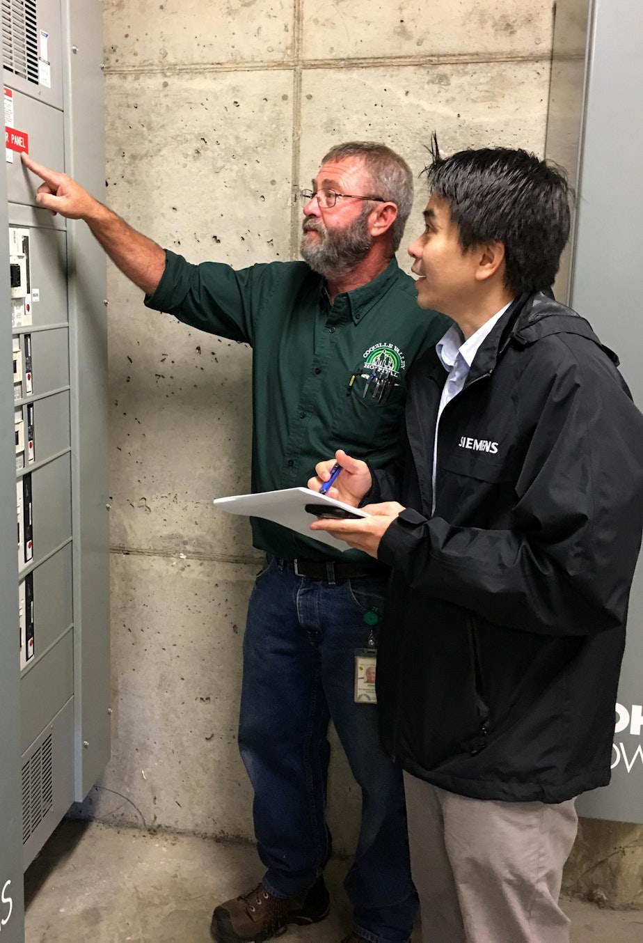 caption: Coquille Valley Hospital plant operations director Ernie Fegles, left, and Andreas Winardi of Siemens discussed how a microgrid might work during a site visit on Sept. 26.