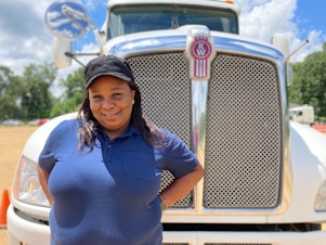 caption: Pamela Williams, a driving instructor with DSC Training Academy, stands in front of one of the academy's trucks on June 29. Williams has been driving for seven years and enjoys seeing the country from the road.