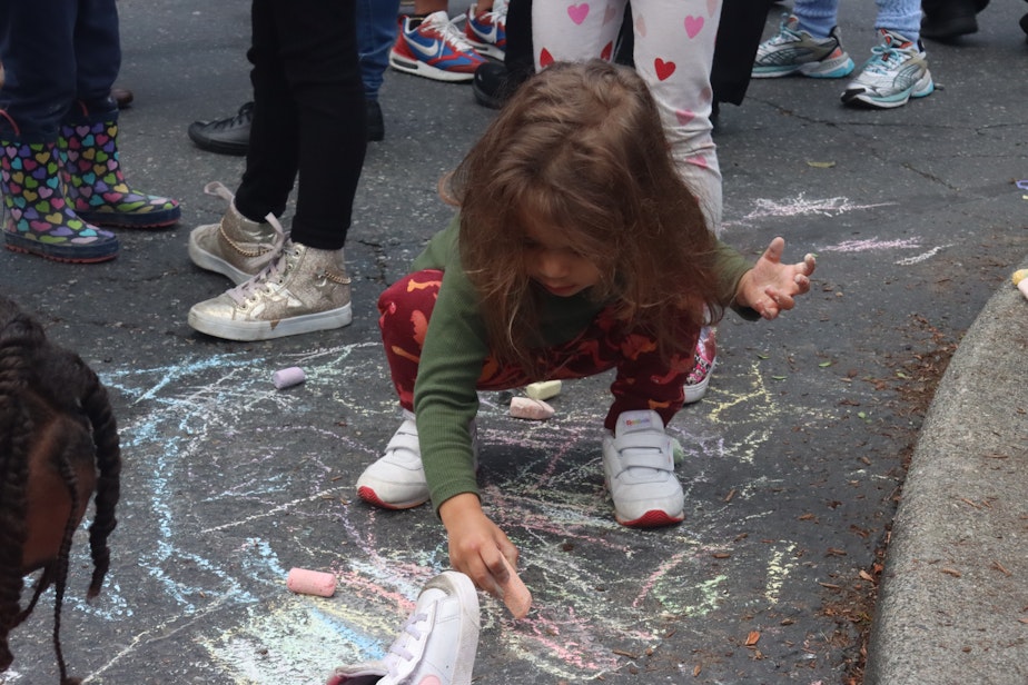 caption: Soleil Justice, who was in the A 4 Apple Learning Center during a shooting, draws with chalk at a rally on Oct. 19, 2023. The rally came after a stray bullet shattered a window at the learning center in Seattle's Central District on Oct. 16.