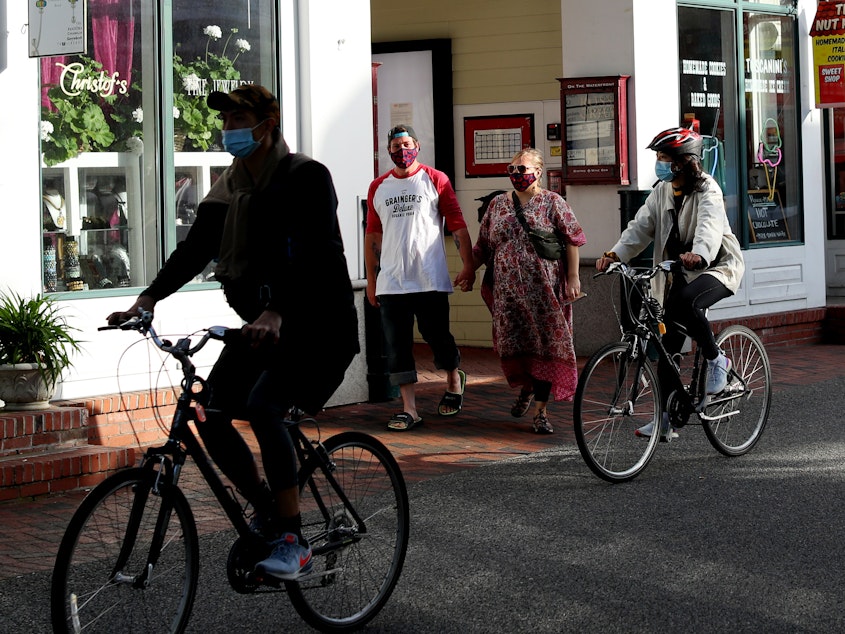 caption: Pedestrians walk down Commercial Street in Provincetown, Mass., in May 2020. A study of a new outbreak in Provincetown found that three-quarters of those infected were fully vaccinated.