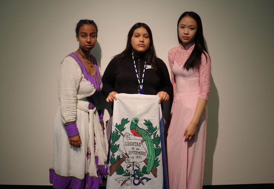 caption: RadioActive's Essey Paulos (left) and Hong Ta (right) wear clothing from their Eritrean and Vietnamese cultures respectively while Michelle Aguilar Ramirez holds the Guatemalan flag.
