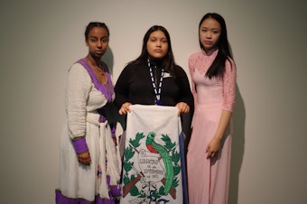 caption: RadioActive's Essey Paulos (left) and Hong Ta (right) wear clothing from their Eritrean and Vietnamese cultures respectively while Michelle Aguilar Ramirez holds the Guatemalan flag.