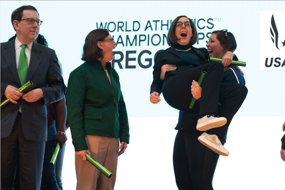 caption: Team USA hammer throw gold medalist DeAnna Price easily lifts Oregon Governor Kate Brown at a kickoff rally Thursday in Eugene for the 2021 World Track and Field Championships.
