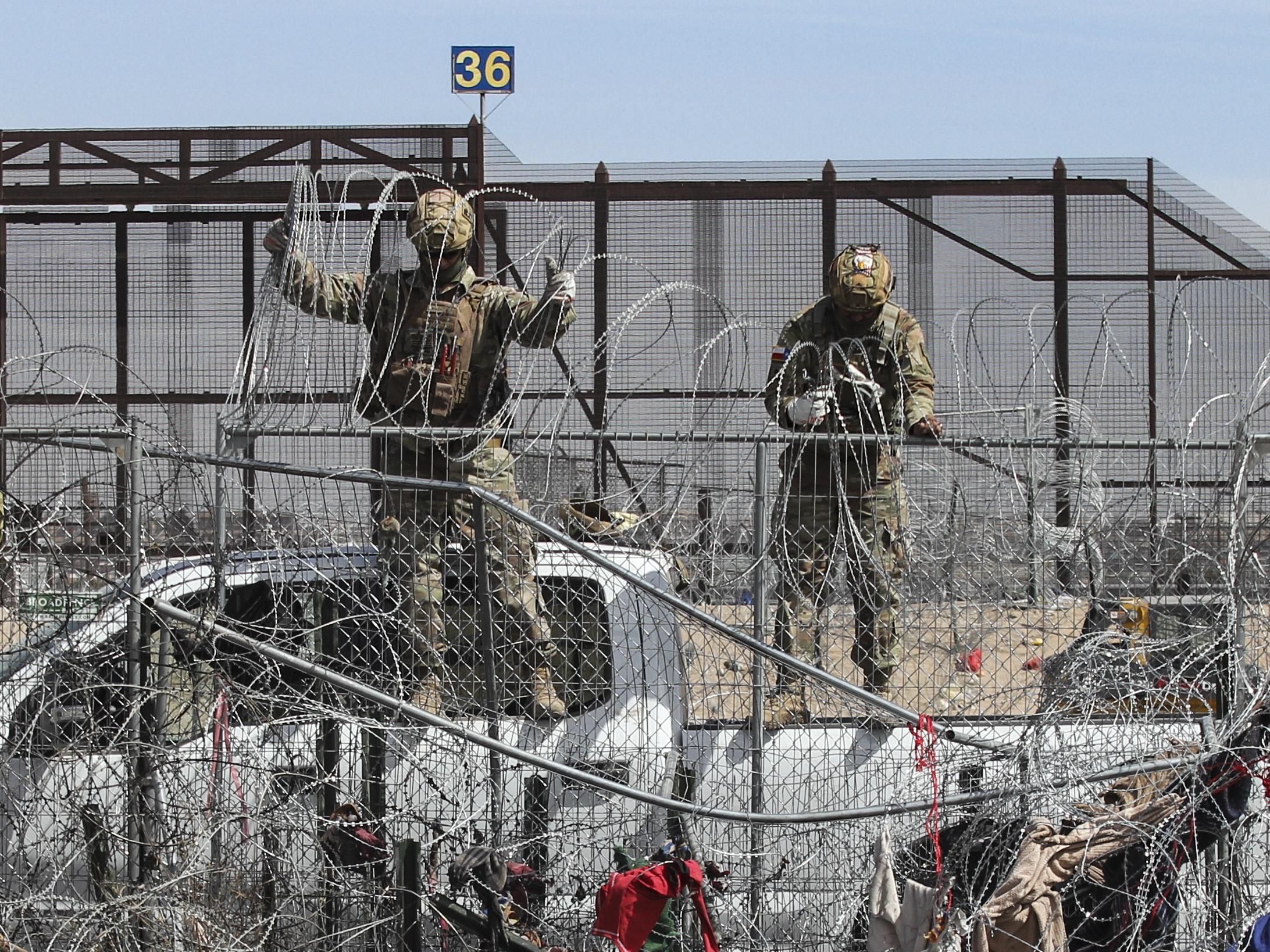 caption: Members of the Texas National Guard placing barber wire on a fence at the border between Mexico and the US.