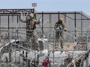 caption: Members of the Texas National Guard placing barber wire on a fence at the border between Mexico and the US.