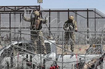 caption: Members of the Texas National Guard placing barber wire on a fence at the border between Mexico and the US.