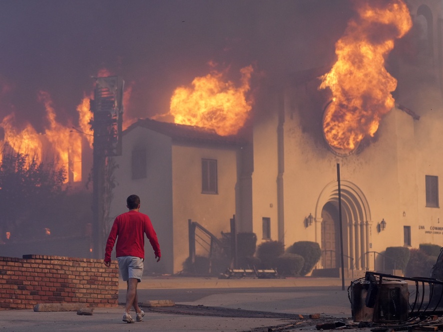 caption: A man walks in front of the burning Altadena Community Church, Wednesday, Jan. 8, 2025, in the downtown Altadena section of Pasadena, Calif.