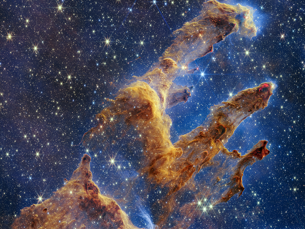 caption: The Pillars of Creation as captured by NASA's James Webb Space Telescope look like arches and spires and are filled with semi-transparent gas and dust. This is a region where young stars are forming.