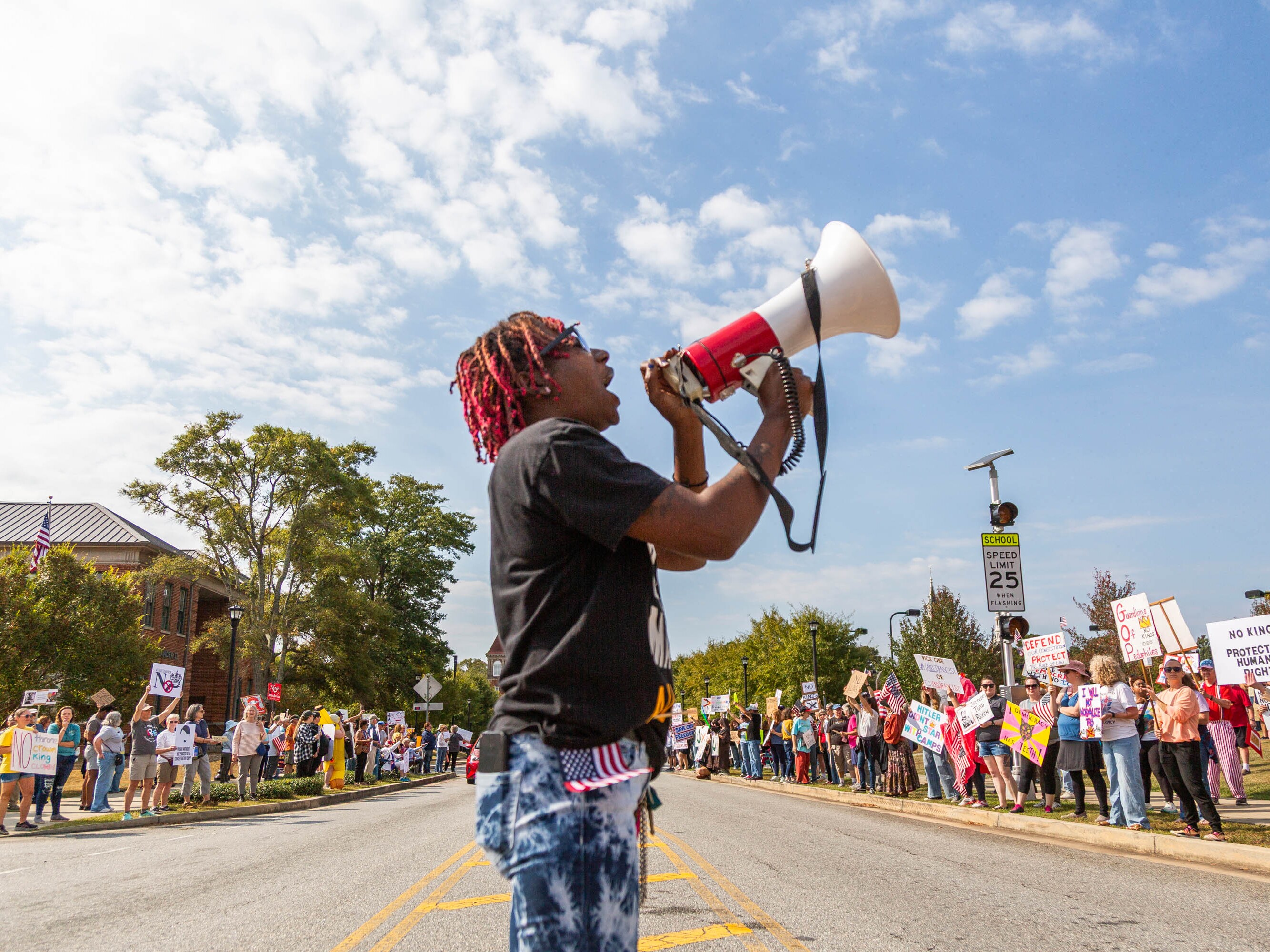 caption: Legacee Medina of Macon, Ga. leads chanting at a No Kings rally between an elementary school and pickleball courts in Macon on October 18, 2025. The rally moved from its earlier location downtown to stay out of the way of a planned Hispanic festival.