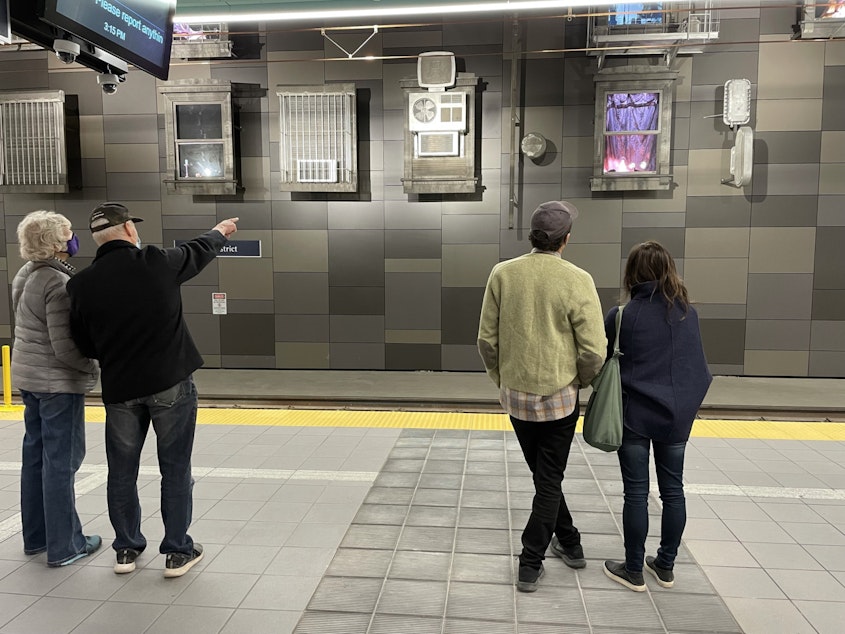 caption: In the U-District station, Annie Han and Daniel Mihalyo of Lead Pencil Studios (right) look at their artwork along with transit riders.