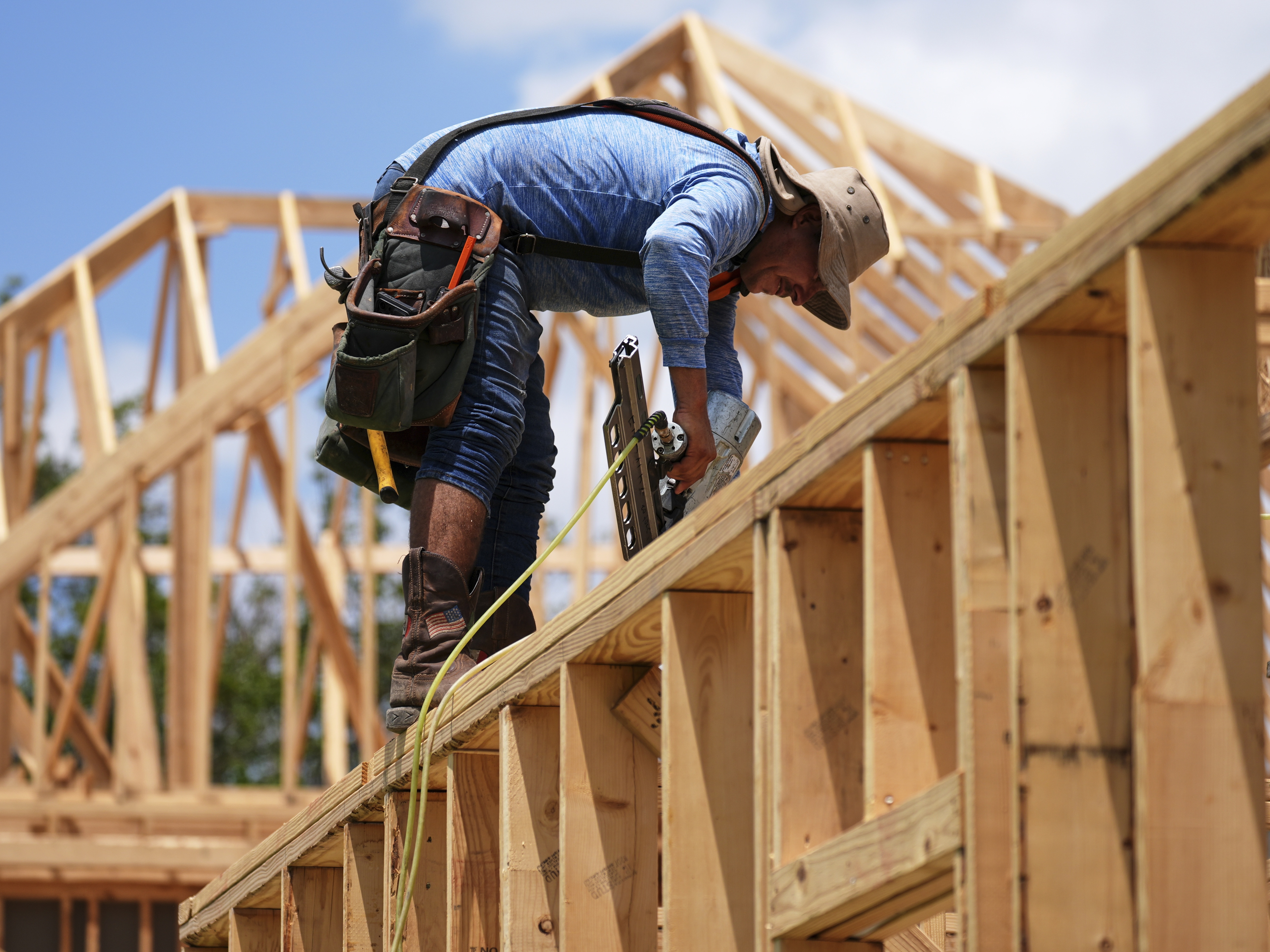 caption: A worker works on the roofing structure of new home under construction, Tuesday, July 15, 2025, in Richardson, Texas.