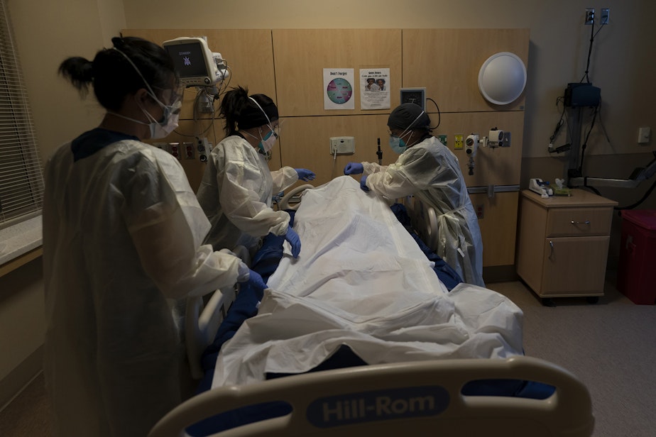 caption: Registered nurse Bryan Hofilena, from right, certified nursing assistant Alexis Figueroa and registered nurse Emily Yu zip up a body bag holding a COVID-19 victim after giving postmortem care at Providence Holy Cross Medical Center in Los Angeles, Tuesday, Dec. 14, 2021. 