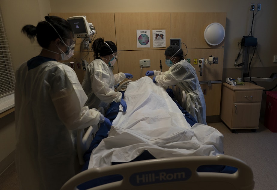 caption: Registered nurse Bryan Hofilena, from right, certified nursing assistant Alexis Figueroa and registered nurse Emily Yu zip up a body bag holding a COVID-19 victim after giving postmortem care at Providence Holy Cross Medical Center in Los Angeles, Tuesday, Dec. 14, 2021. 