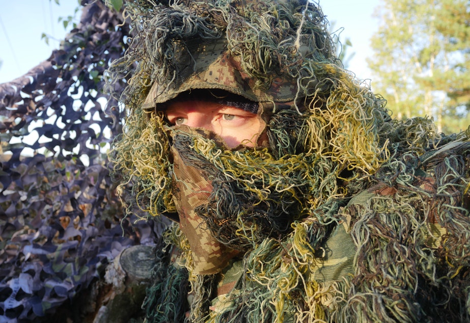 caption: Chris Morgan wearing a ghillie suit as he waits for wolves in Germany.