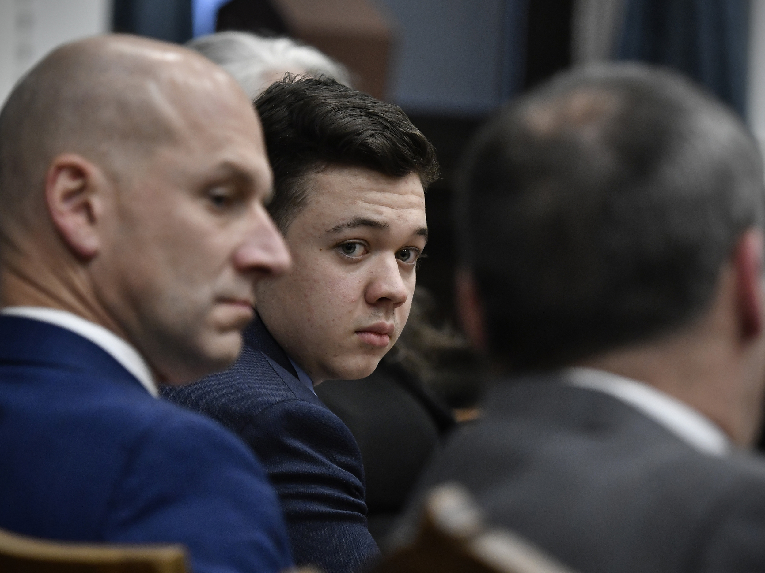 caption: Kyle Rittenhouse, center, looks over to his attorneys as the jury is dismissed for the day during his trial at the Kenosha County Courthouse on Thursday in Kenosha, Wisconsin.