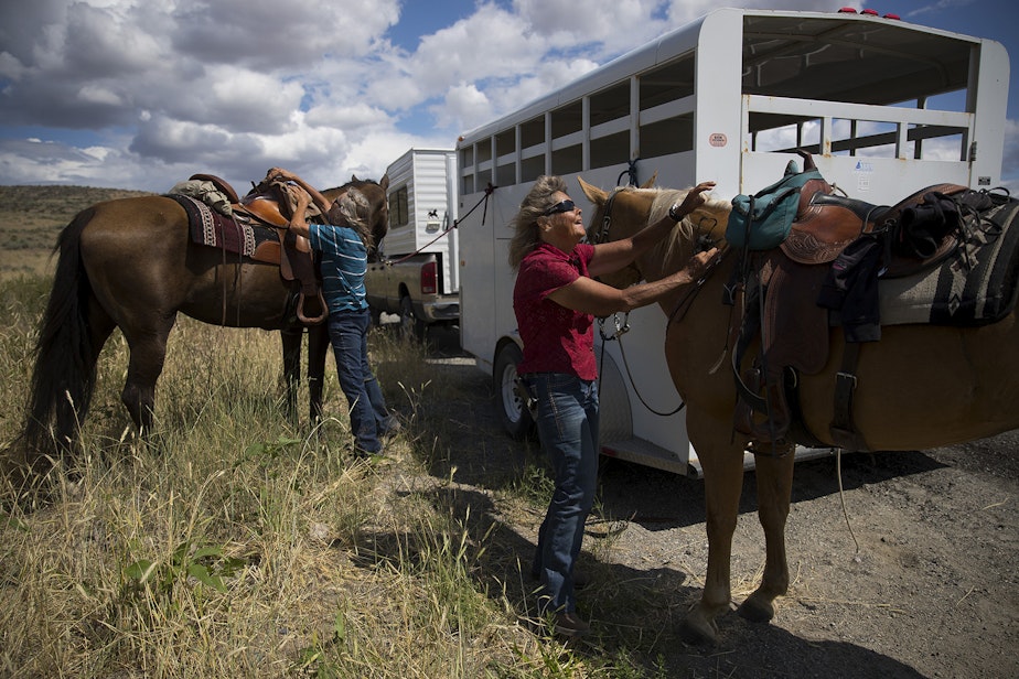 caption: Sue Robbins, left, and Julie Hensley, right, take the saddles off of their horses, Mocha and Hot Rod, after riding near the ranch where Julie grew up, on Tuesday, July 16, 2019, near Brewster.